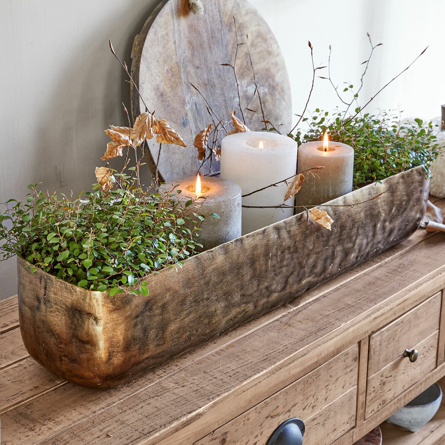 Schaal Skye Decoratieve gouden metalen plantenbak met groene planten en drie kaarsen op houten tafel