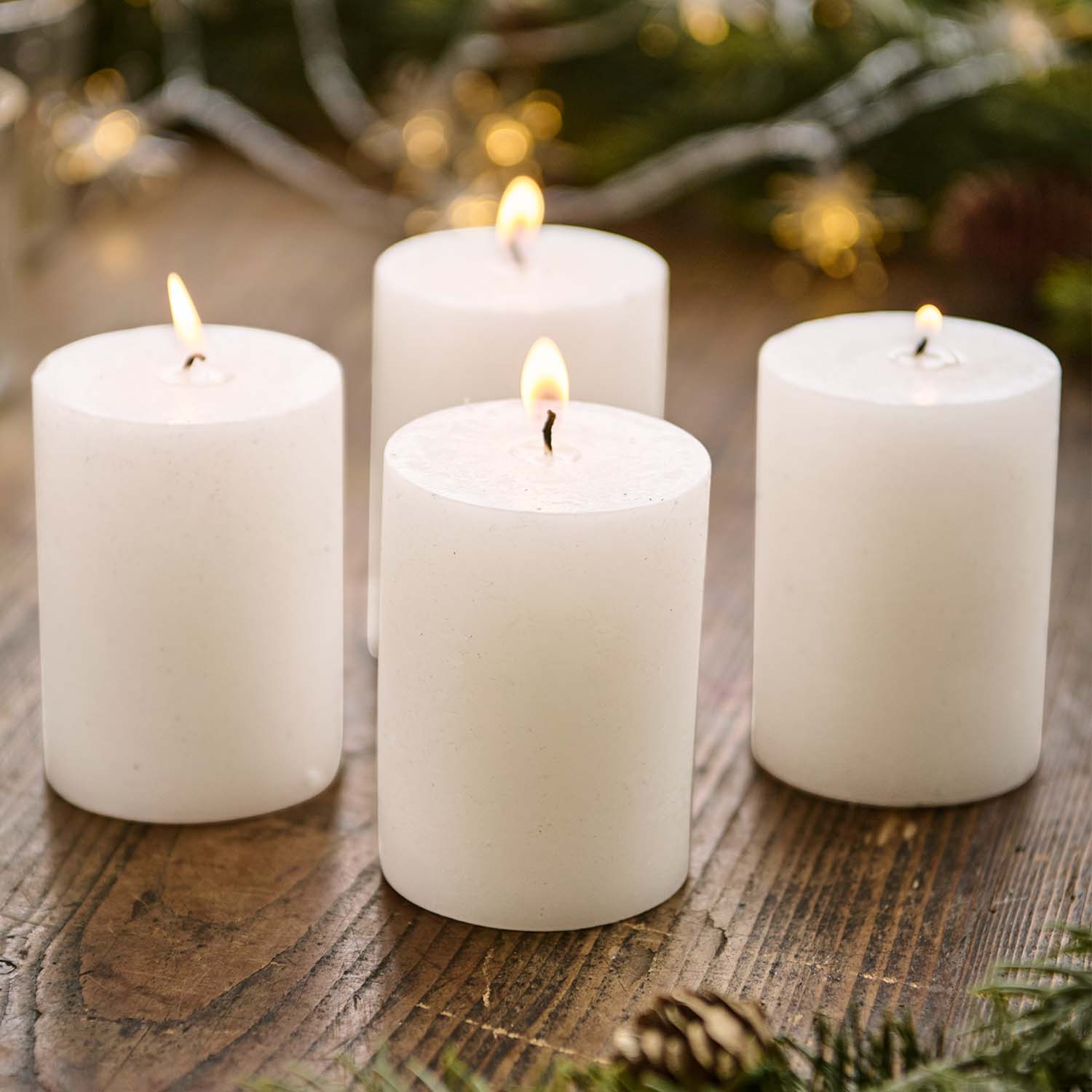 Set van vier witte stompkaarsen op houten tafel met kerstdecoratie op de achtergrond