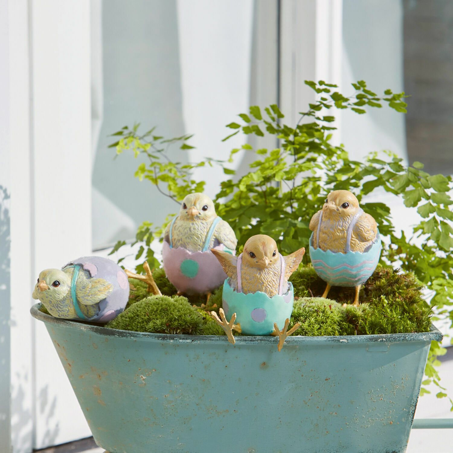 Figurines décoratives de poussins dans des coquilles pastel sur mousse verte dans une brouette bleue