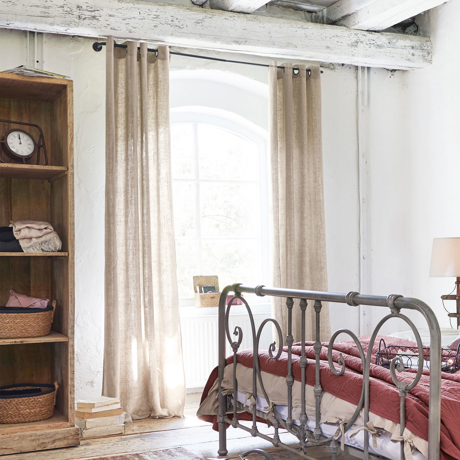 Slaapkamer met metalen bed en beige gordijnen van natuurlijk linnen in rustieke stijl