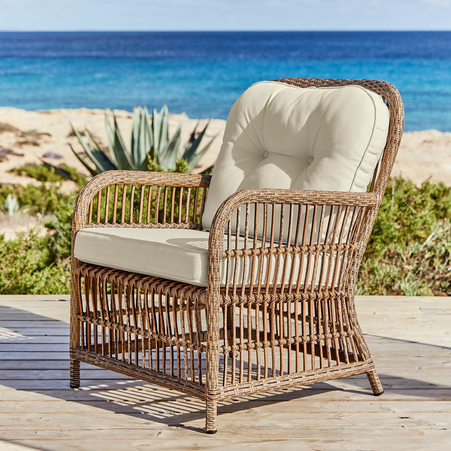 Fauteuil en rotin avec coussins crème sur terrasse en bois face à la mer, mobilier extérieur