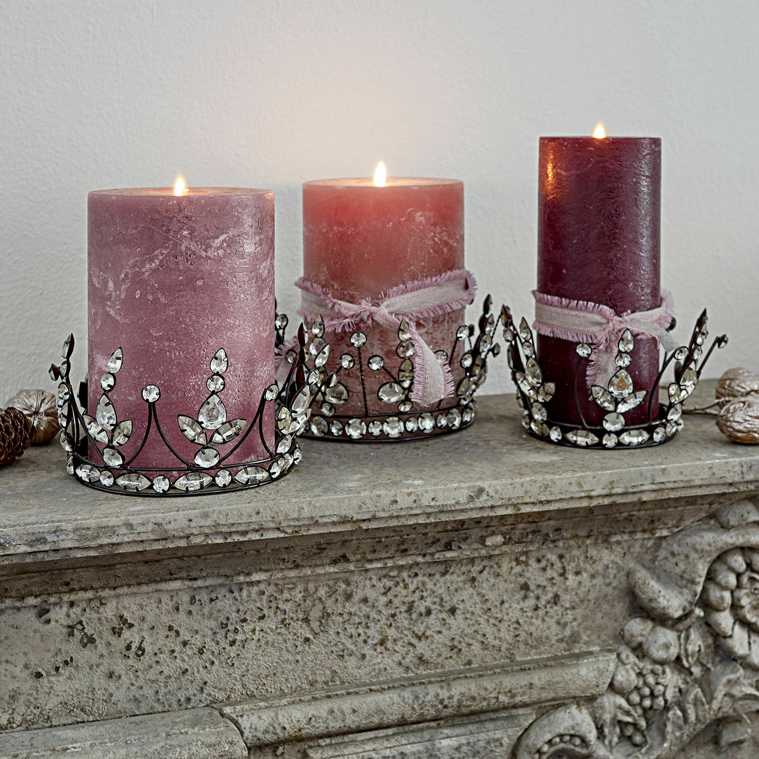 Sierkroon set van 3 Bigas Drie roze decoratieve kaarsen met metalen houders versierd met kristallen op een stenen schoorsteenmantel