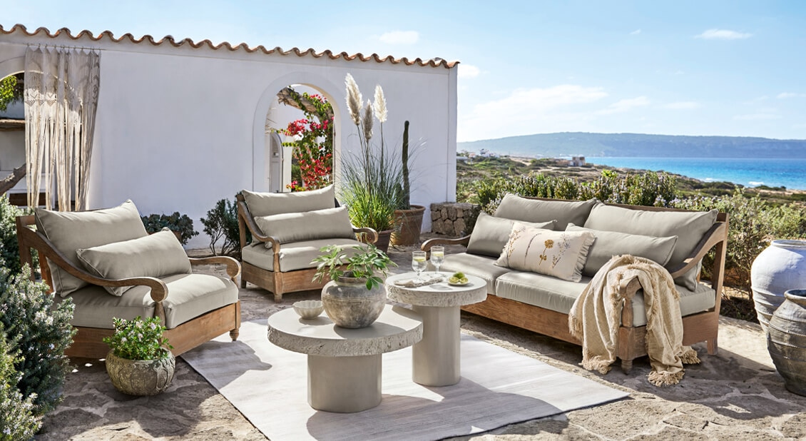 Tuinmeubelset van hout met beige kussens op stenen terras met uitzicht op zee