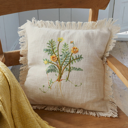 Beige linnen kussen met franjes en geborduurd bloemenmotief op houten stoel