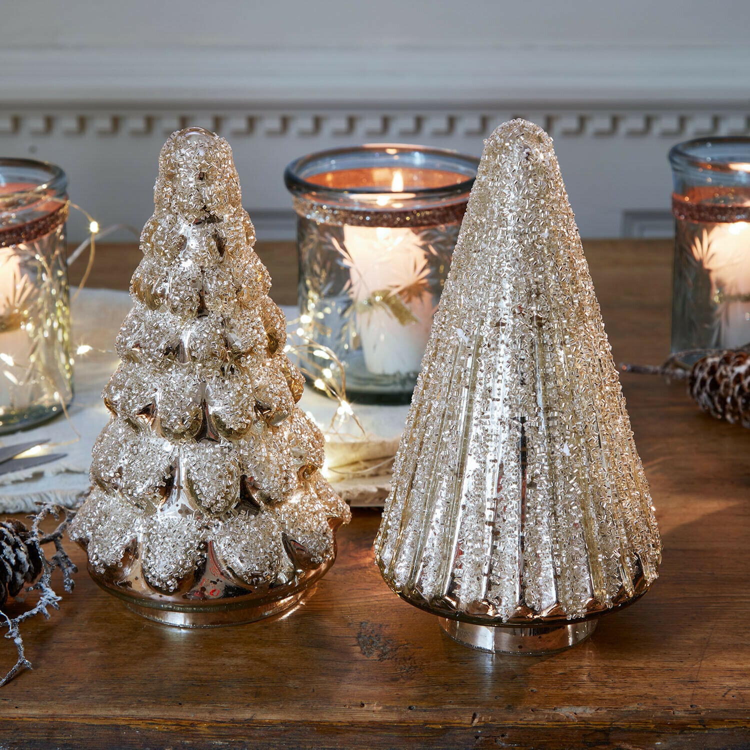 Decoratieve boom set van 2 Domélys Twee decoratieve gouden glazen kerstbomen met textuur op houten tafel met lantaarns en kaarslicht