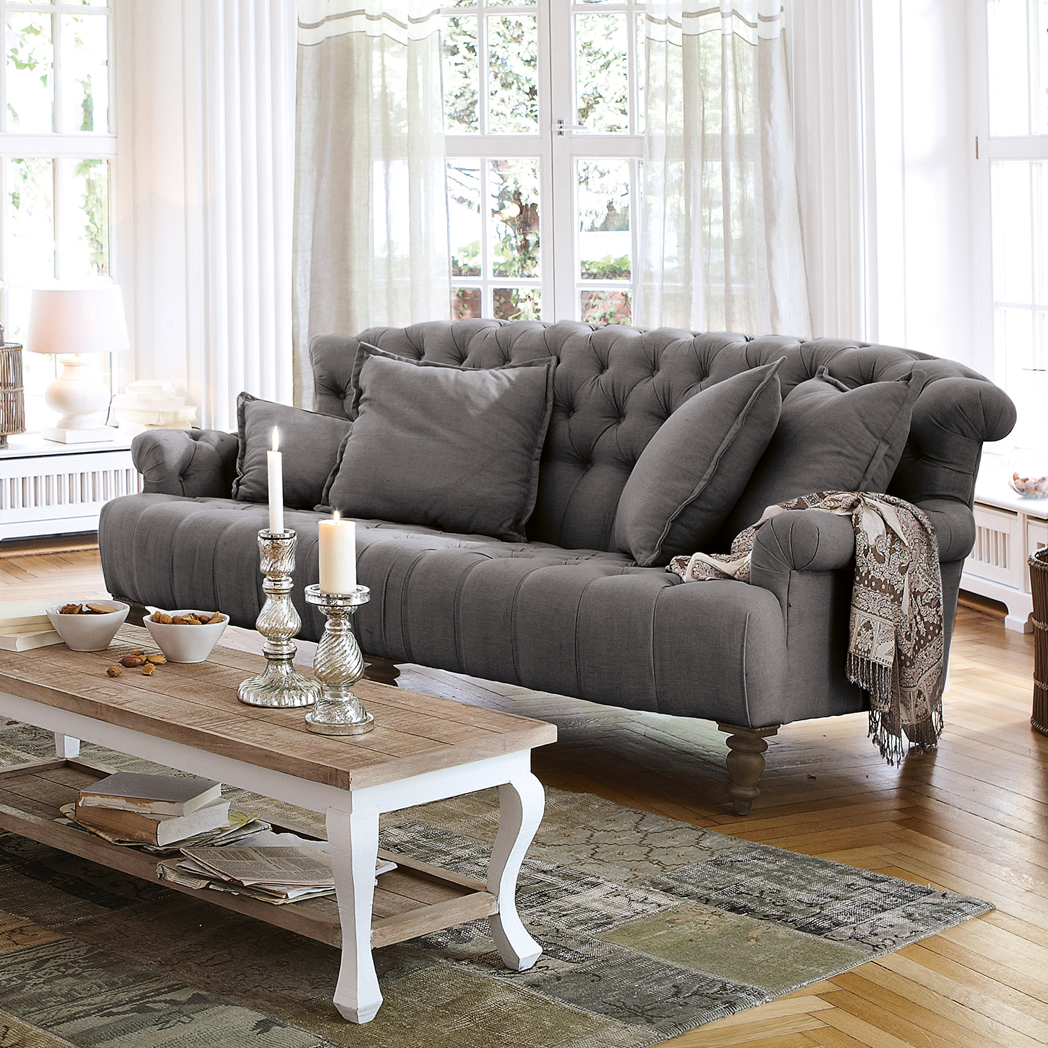 Grijze gestoffeerde stoffen bank met kussens en decoratief plaid in lichte woonkamer met houten vloer