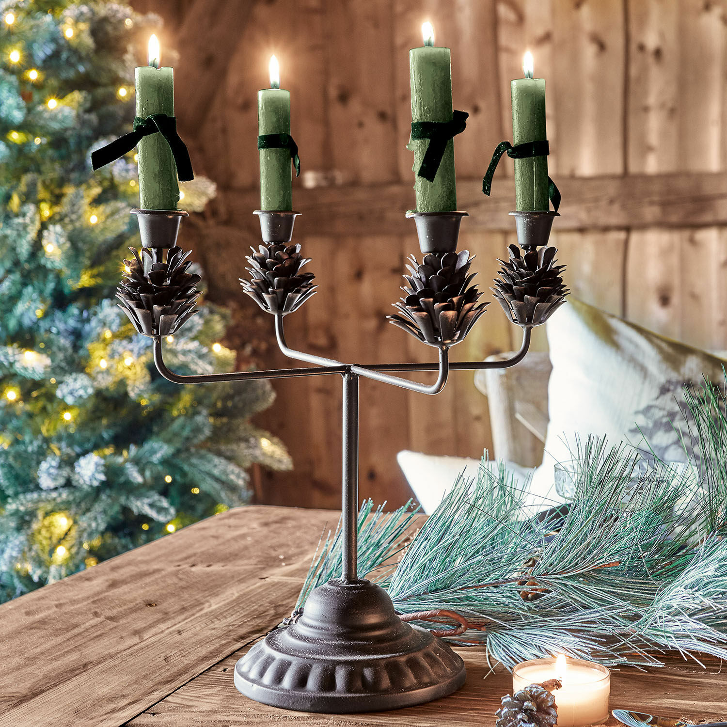 Chandelier en métal avec quatre bougies vertes et décorations pommes de pin sur table en bois