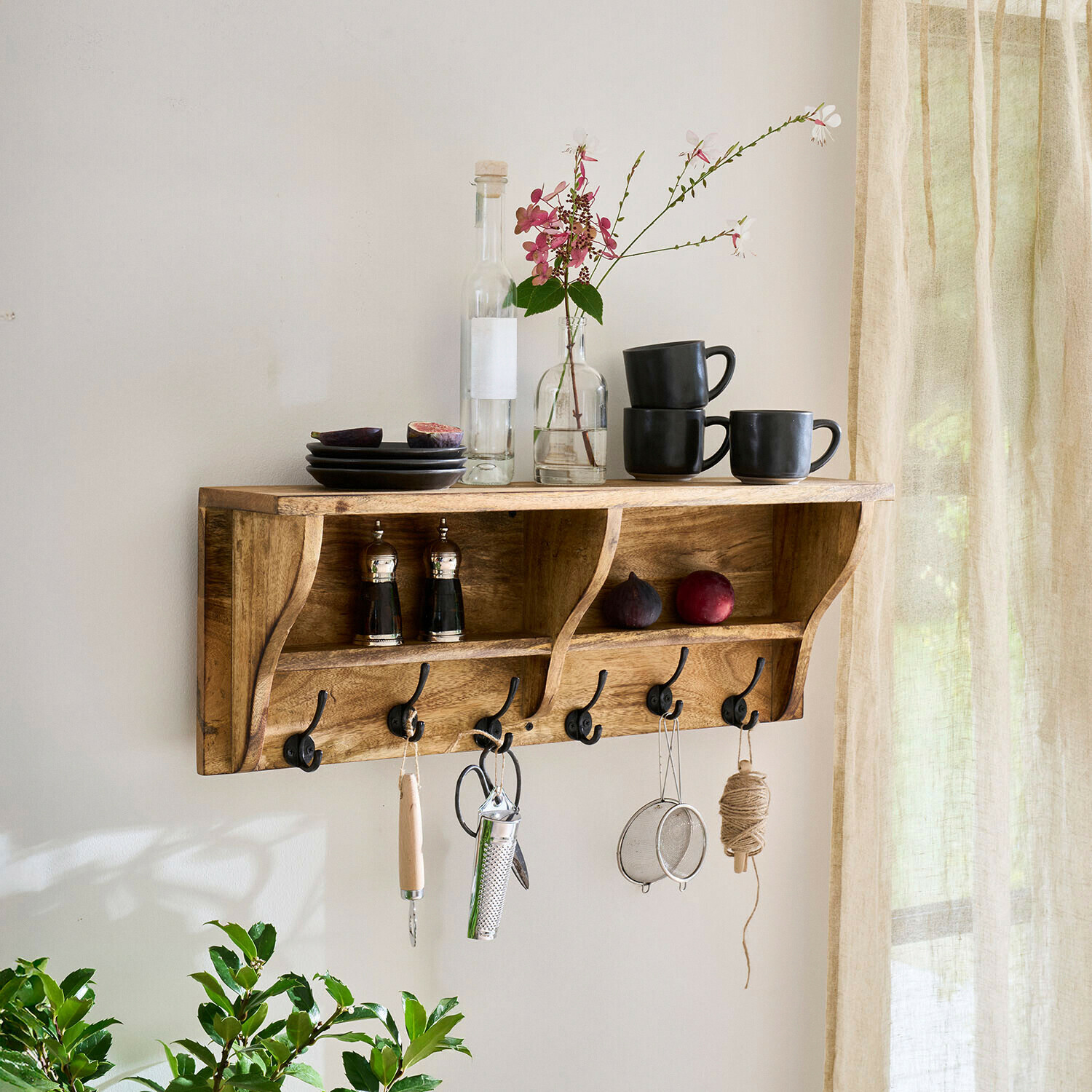 Étagère murale en bois avec crochets, tasses noires, assiettes et décoration florale dans un intérieur lumineux