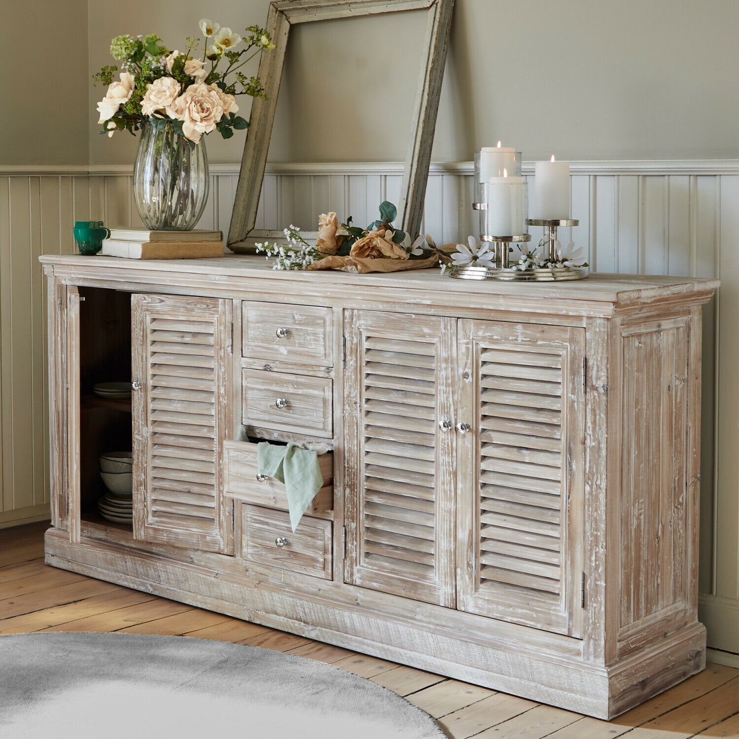 Rustieke houten dressoir met witgewassen afwerking, bloemen en kaarsen in een woonkamer