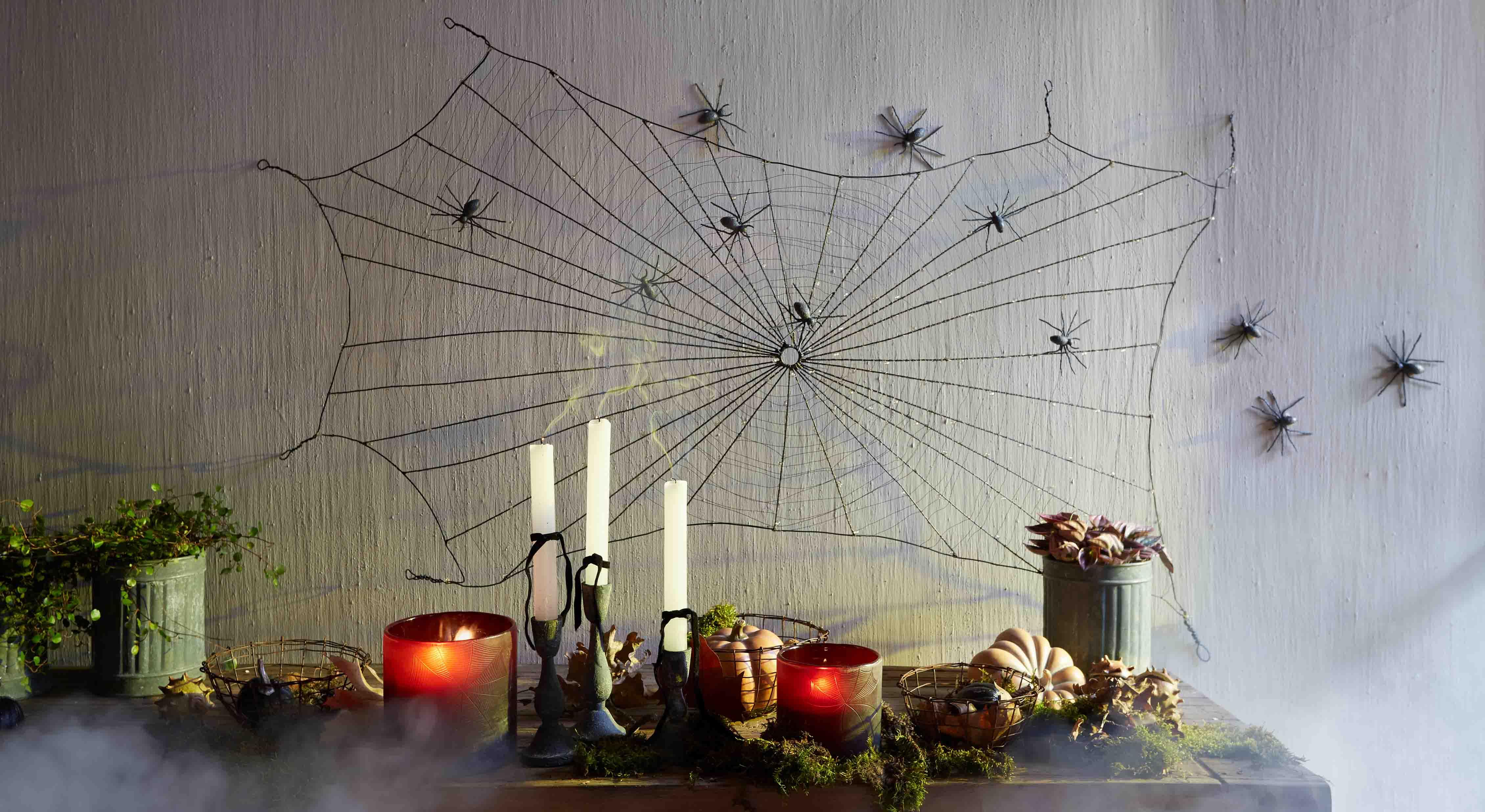 Décoration Halloween avec toile d'araignée noire et araignées en plastique sur le mur, bougies et citrouilles sur la table