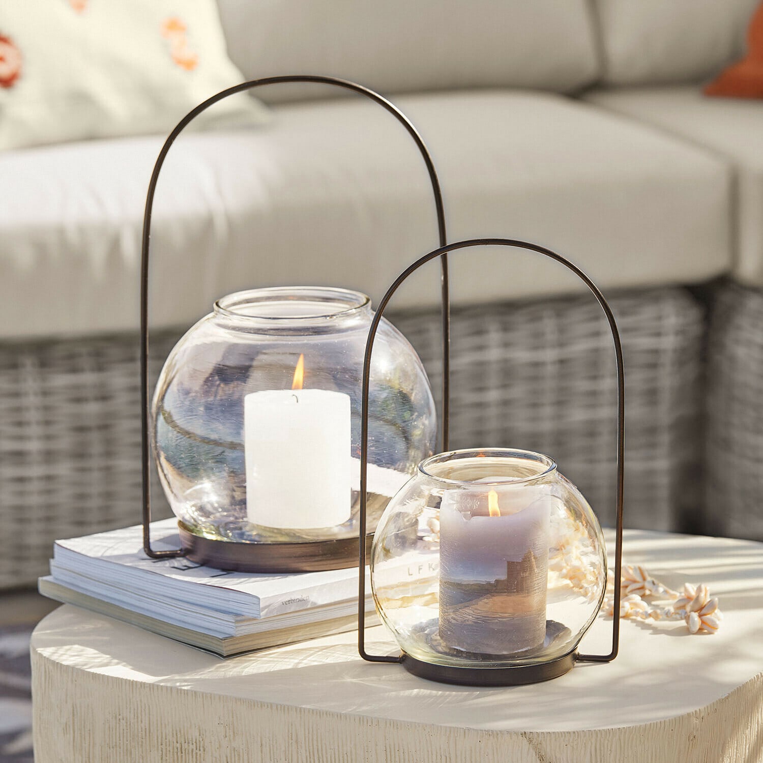 Deux lanternes en verre avec poignées métalliques et bougies allumées sur une table claire décorative