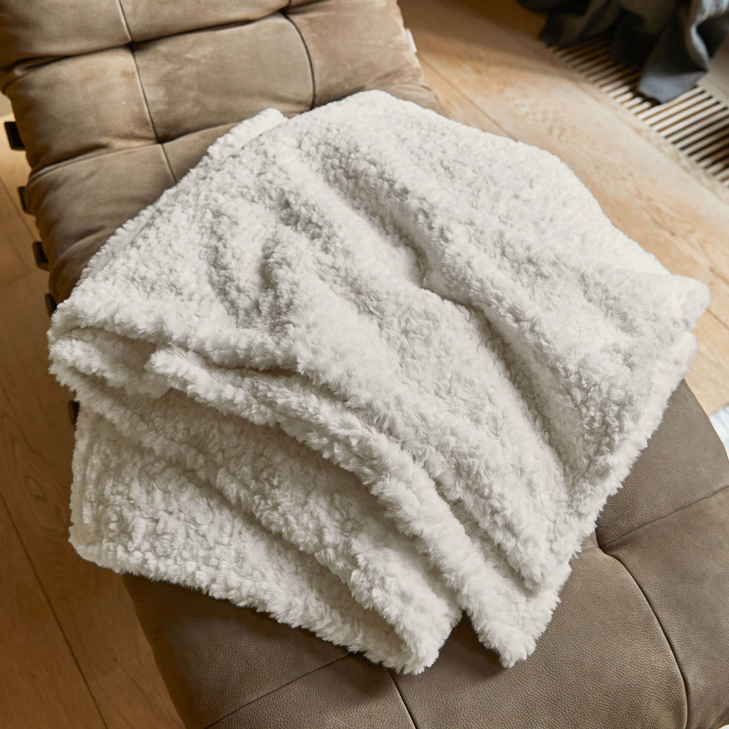 Plaid blanc doux en matière pelucheuse posé sur un fauteuil marron, parfait pour le salon