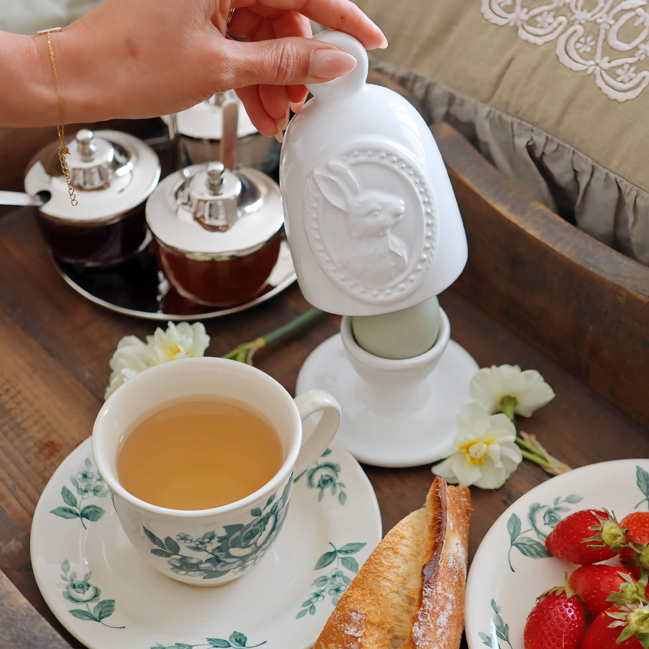 Witte keramische pot met konijnenmotief op ontbijttafel met thee en aardbeien