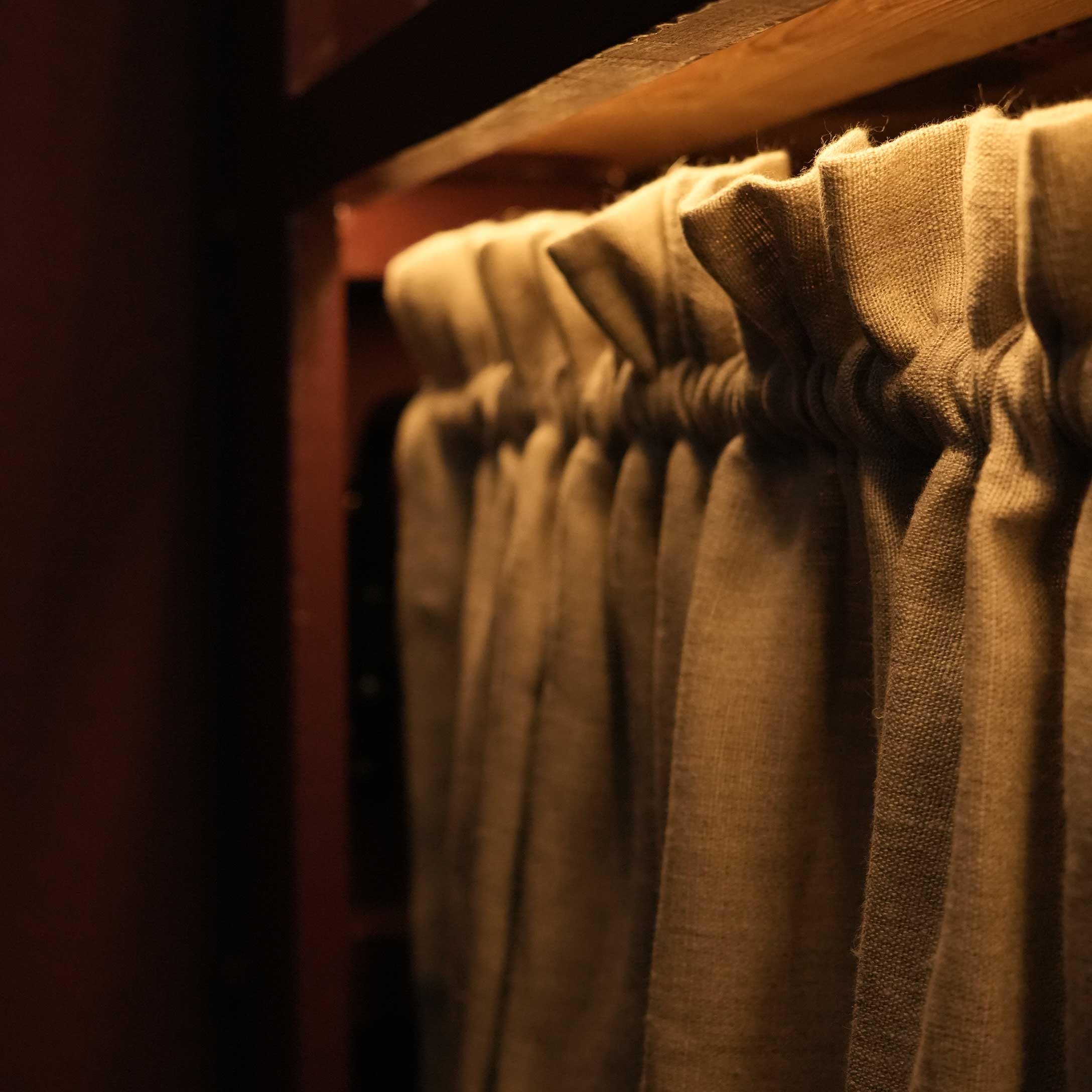 Beige linnen gordijn met plooien aan houten roede in warm licht