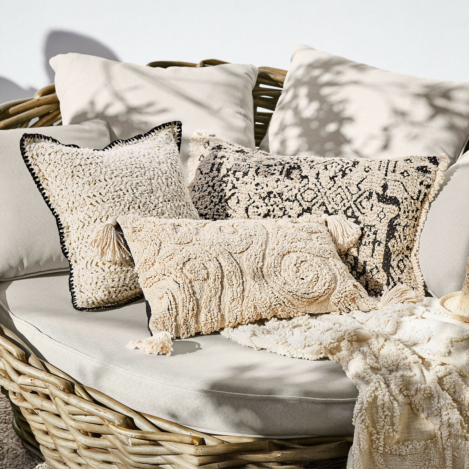 Set crème decoratieve kussens van zacht materiaal op rotan bank, boho stijl