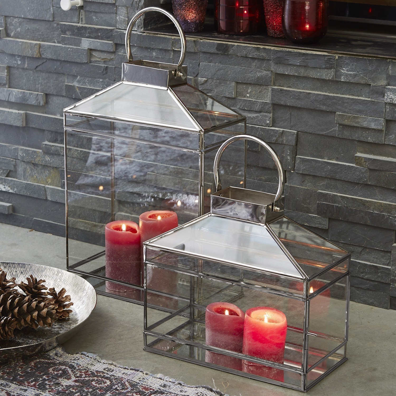 Glazen lantaarns met metalen frame en rode kaarsen voor stenen muur, sfeervolle woondecoratie