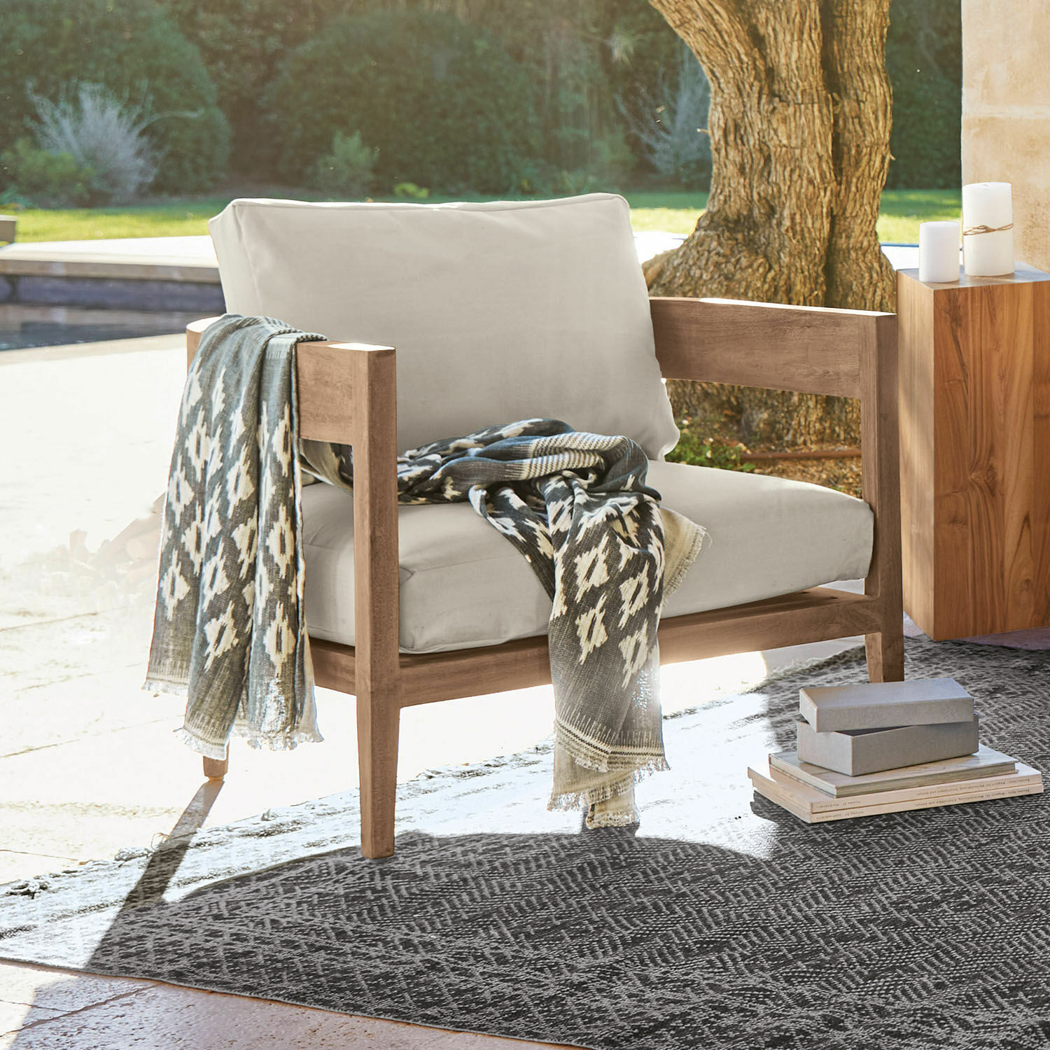 Fauteuil avec coussins beige clair et structure en bois, plaid gris à motifs posé dessus en extérieur