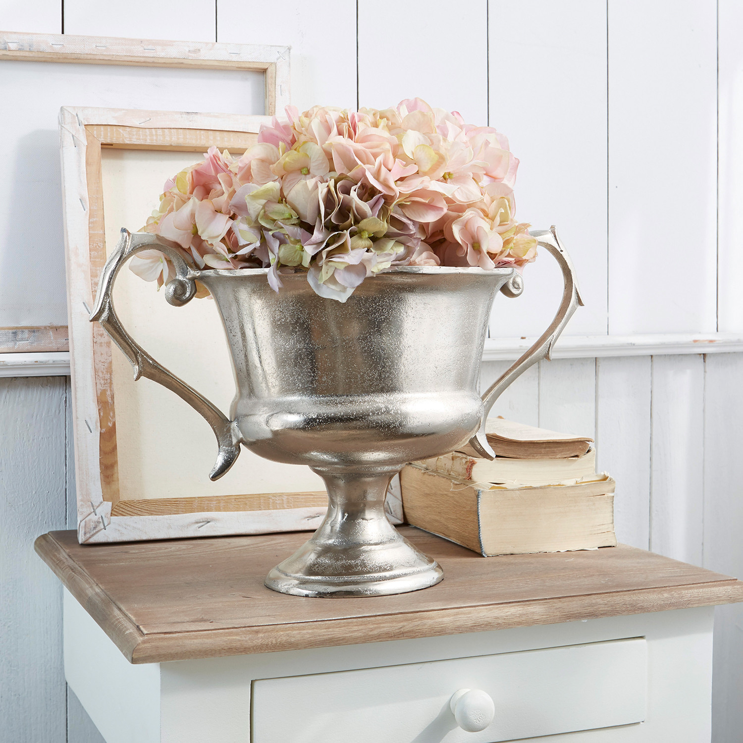 Coupe en métal argenté avec poignées et fleurs roses sur table en bois, décoration intérieure
