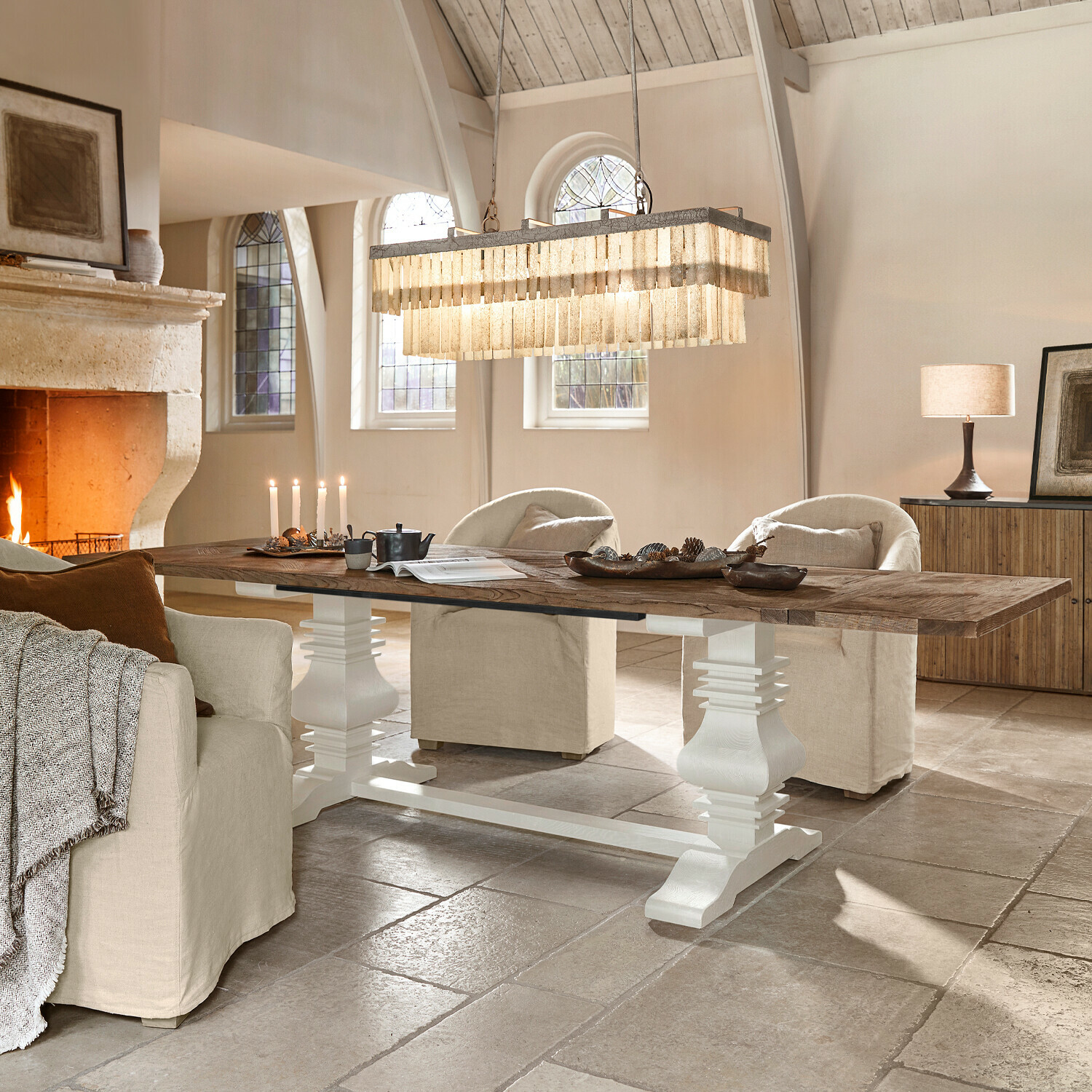 Grande table en bois avec pied blanc dans un salon lumineux avec cheminée et fauteuils beige