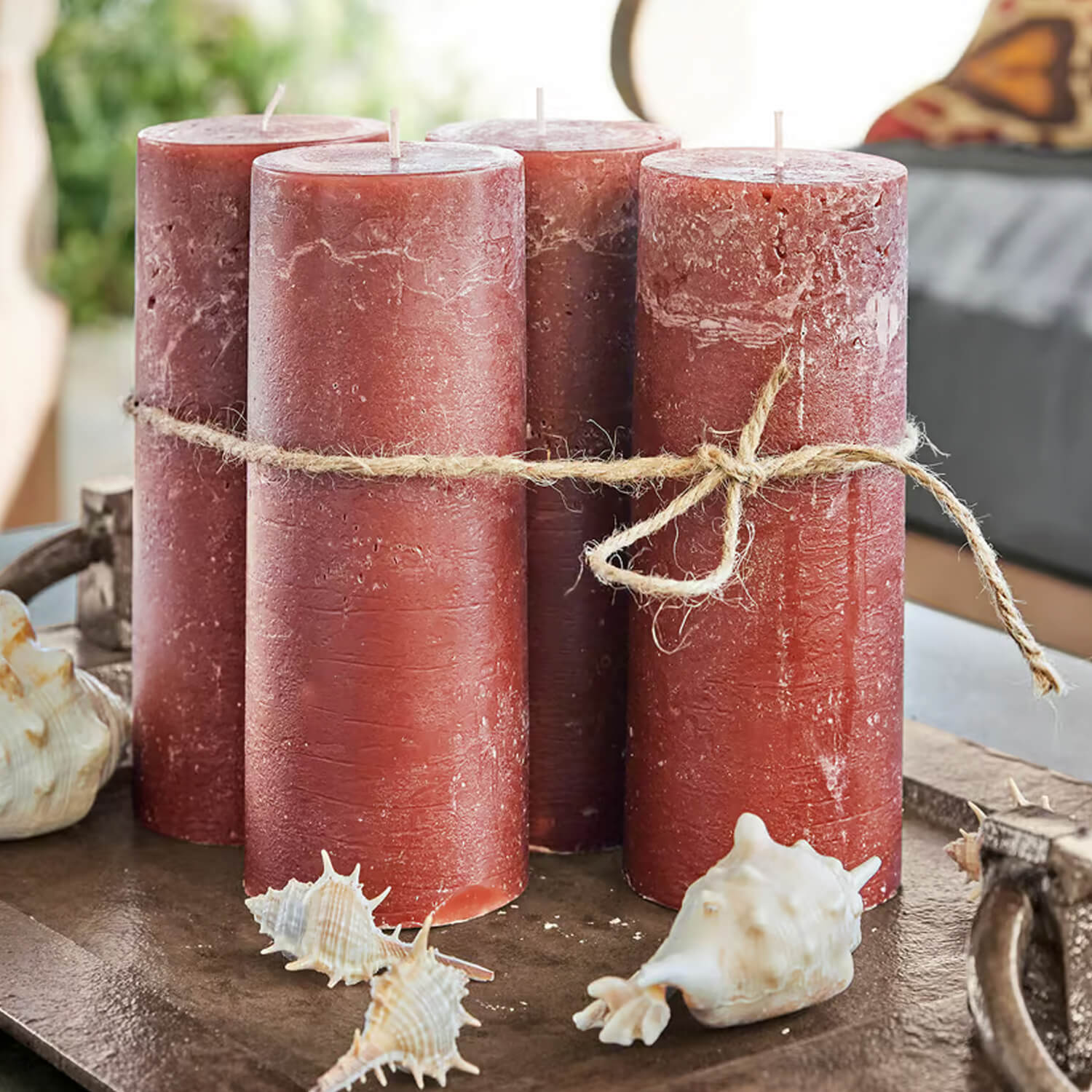 Quatre bougies rouges en cire liées par une corde naturelle sur un plateau décoré de coquillages