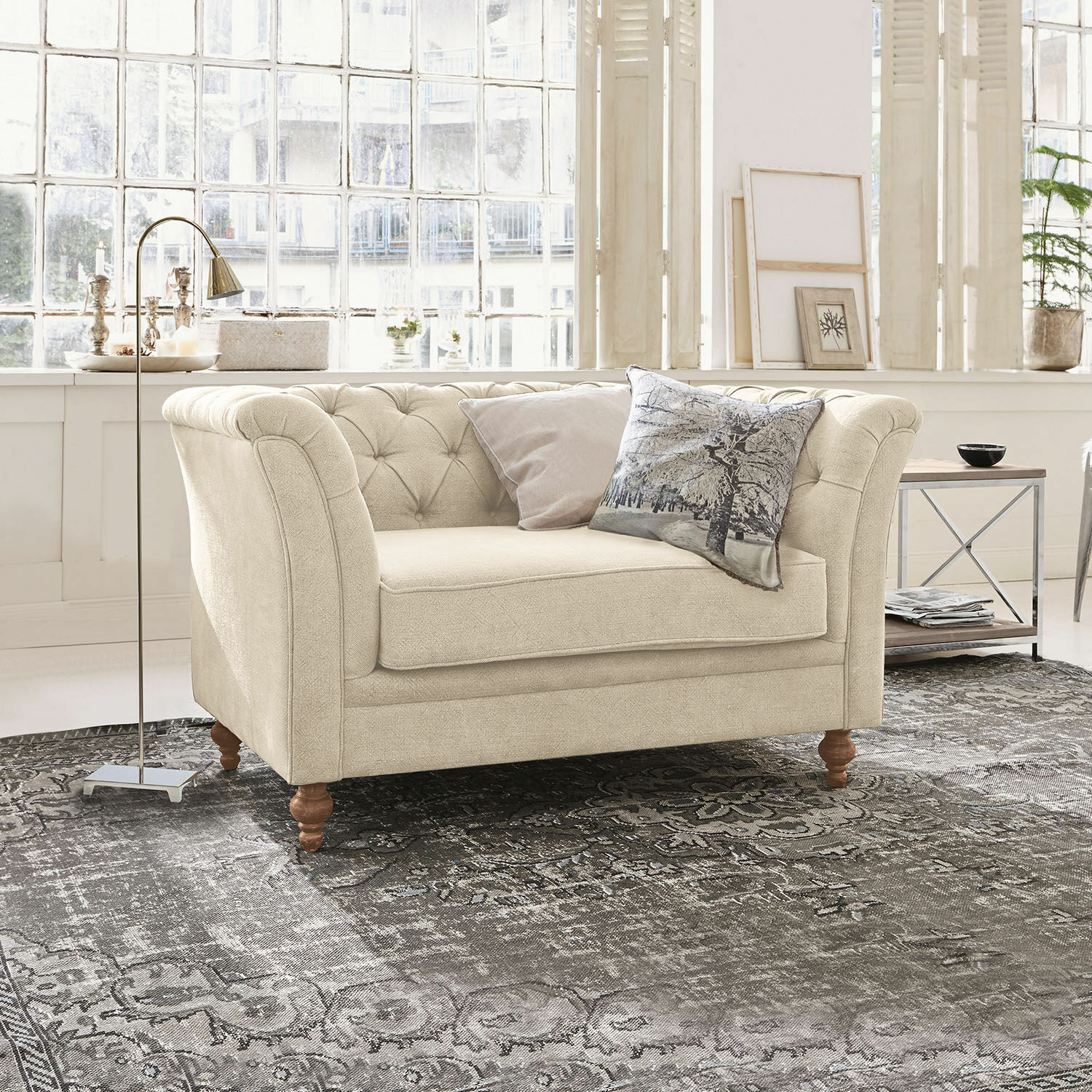 Bank Clères Beige stoffen bank met gestikte rugleuning en houten poten op een grijs vloerkleed in lichte kamer