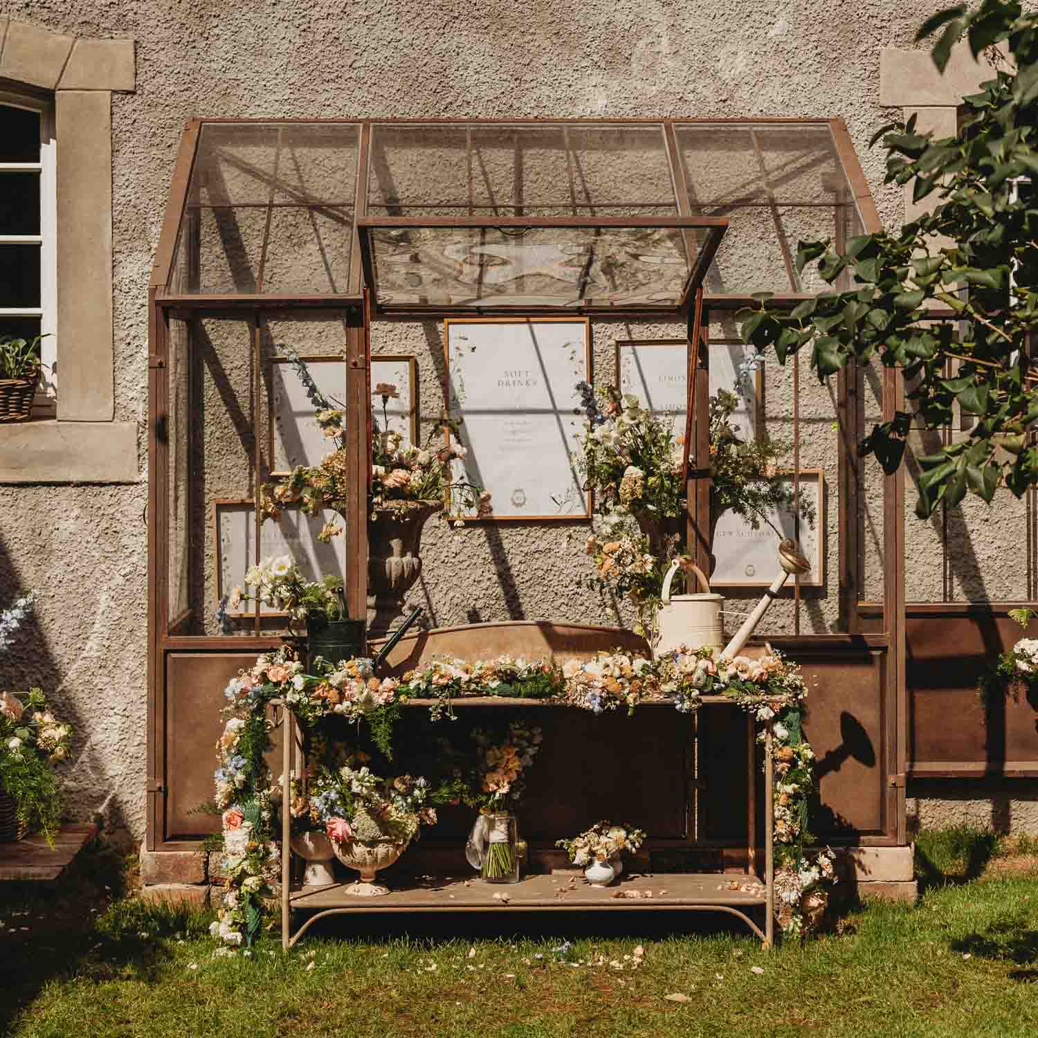 Rustieke metalen tuinbank met bloemen en gieter voor een gestructureerde muur met raam