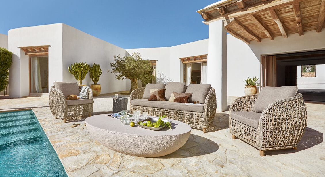 Ensemble de mobilier d'extérieur en rotin beige avec coussins gris au bord d'une piscine sur une terrasse en pierre