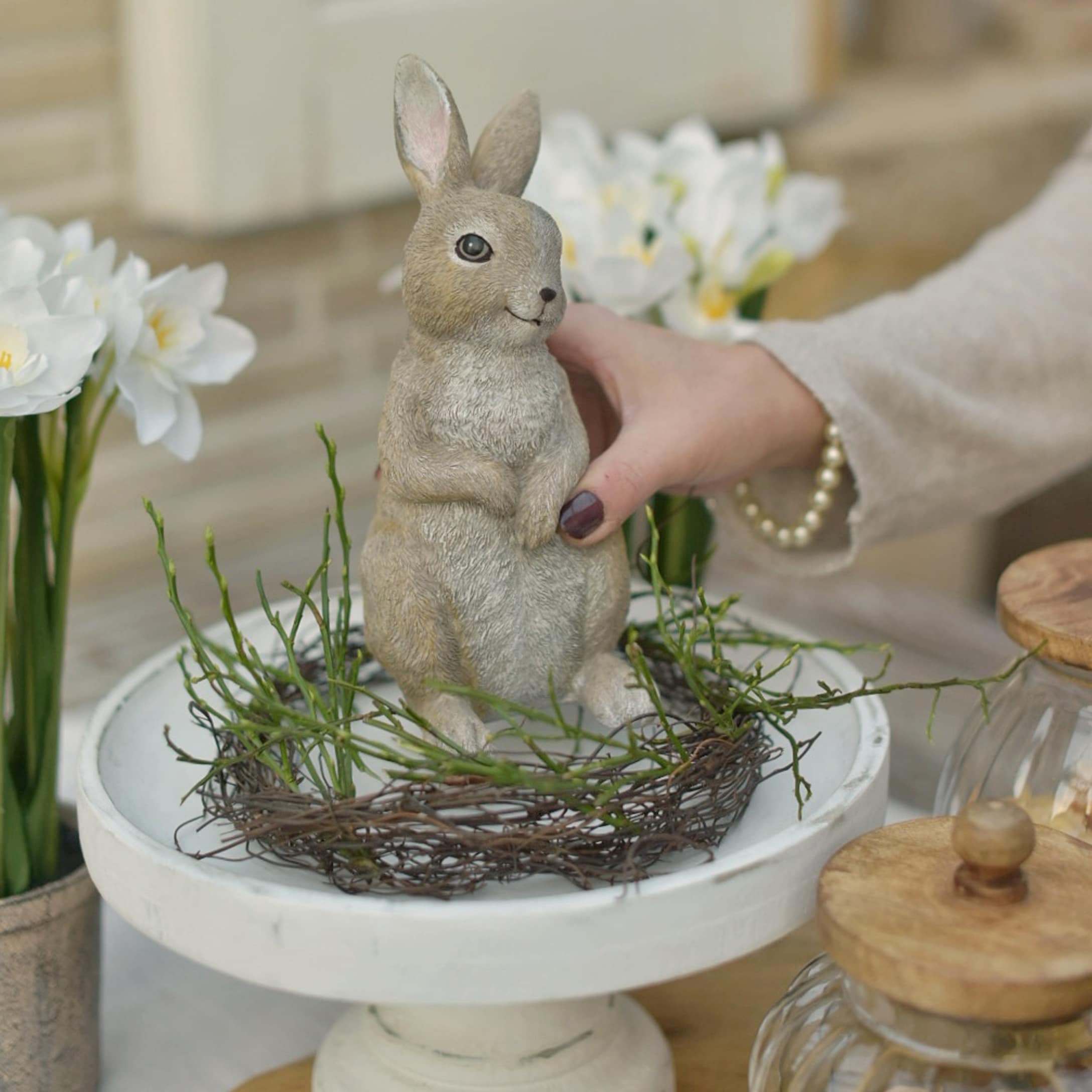Lapin décoratif de Pâques en matériau naturel beige sur un socle blanc avec branches vertes