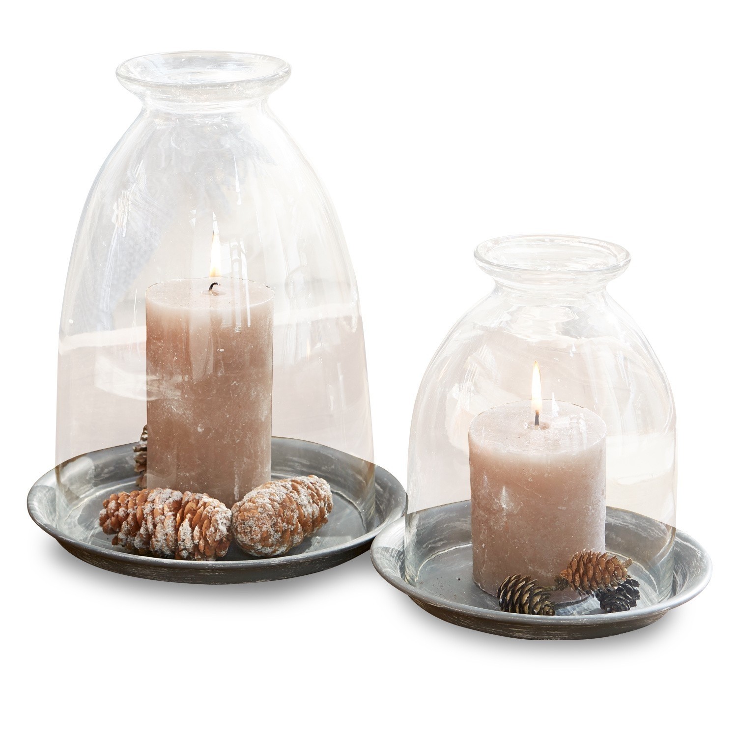 Ensemble de deux bougies sous cloches en verre sur plateaux métalliques avec pommes de pin décoratives