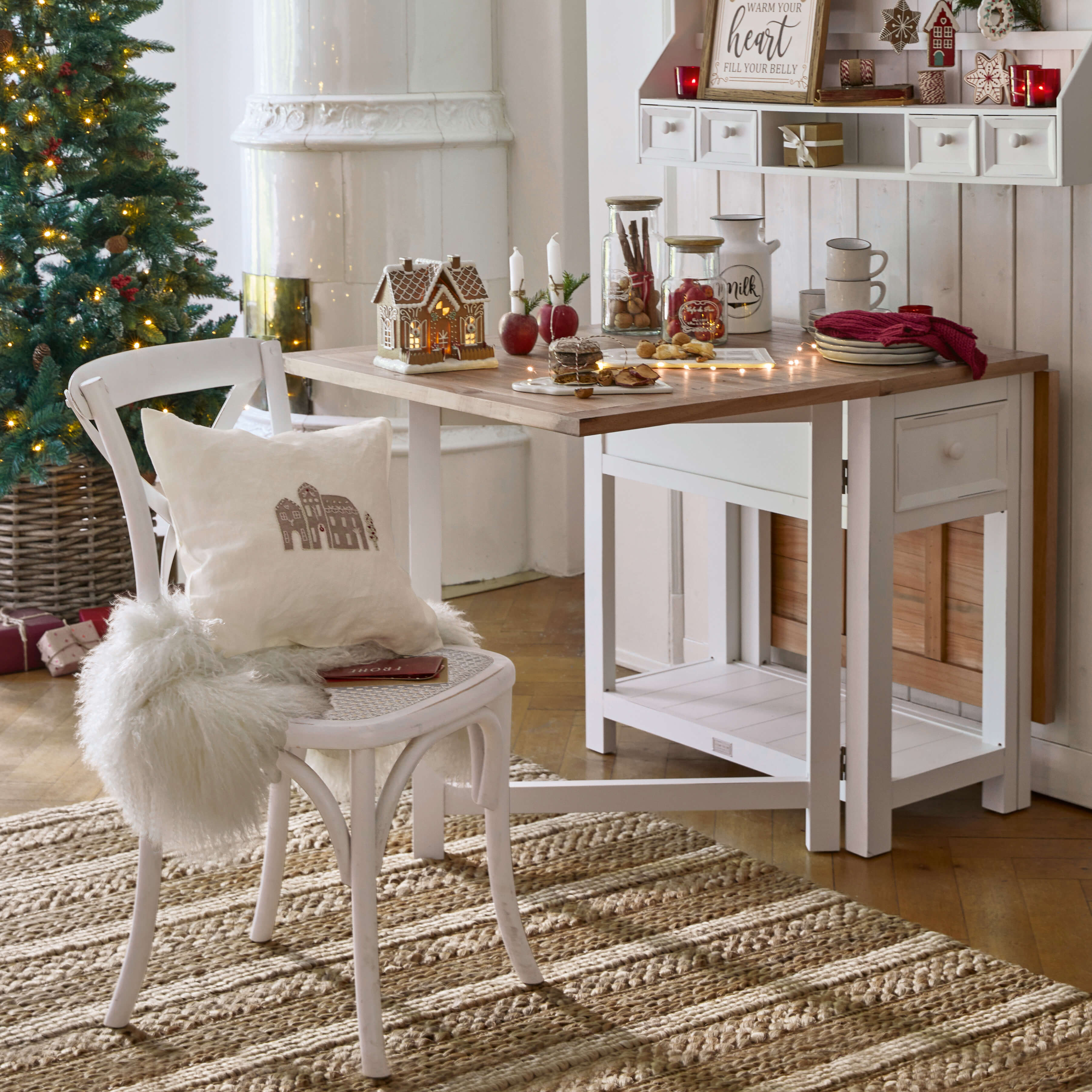 Table et chaise en bois blanc avec décorations de Noël et sapin illuminé dans un intérieur chaleureux