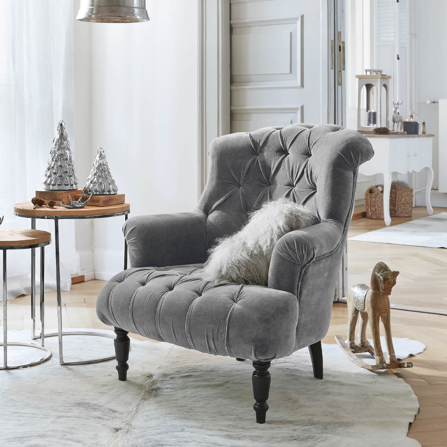 Grijze fluwelen fauteuil met gestikte rugleuning en zwarte poten in lichte woonkamer met kerstdecoratie
