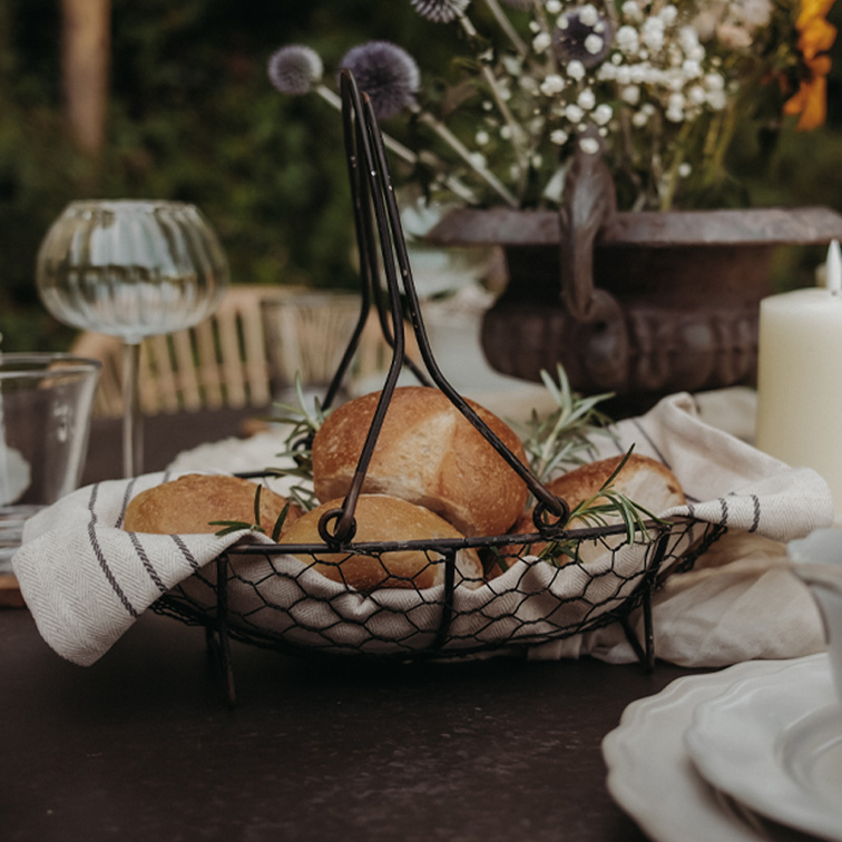 Metalen broodmand met handvatten, bekleed met linnen doek, gevuld met broodjes en kruiden op tafel