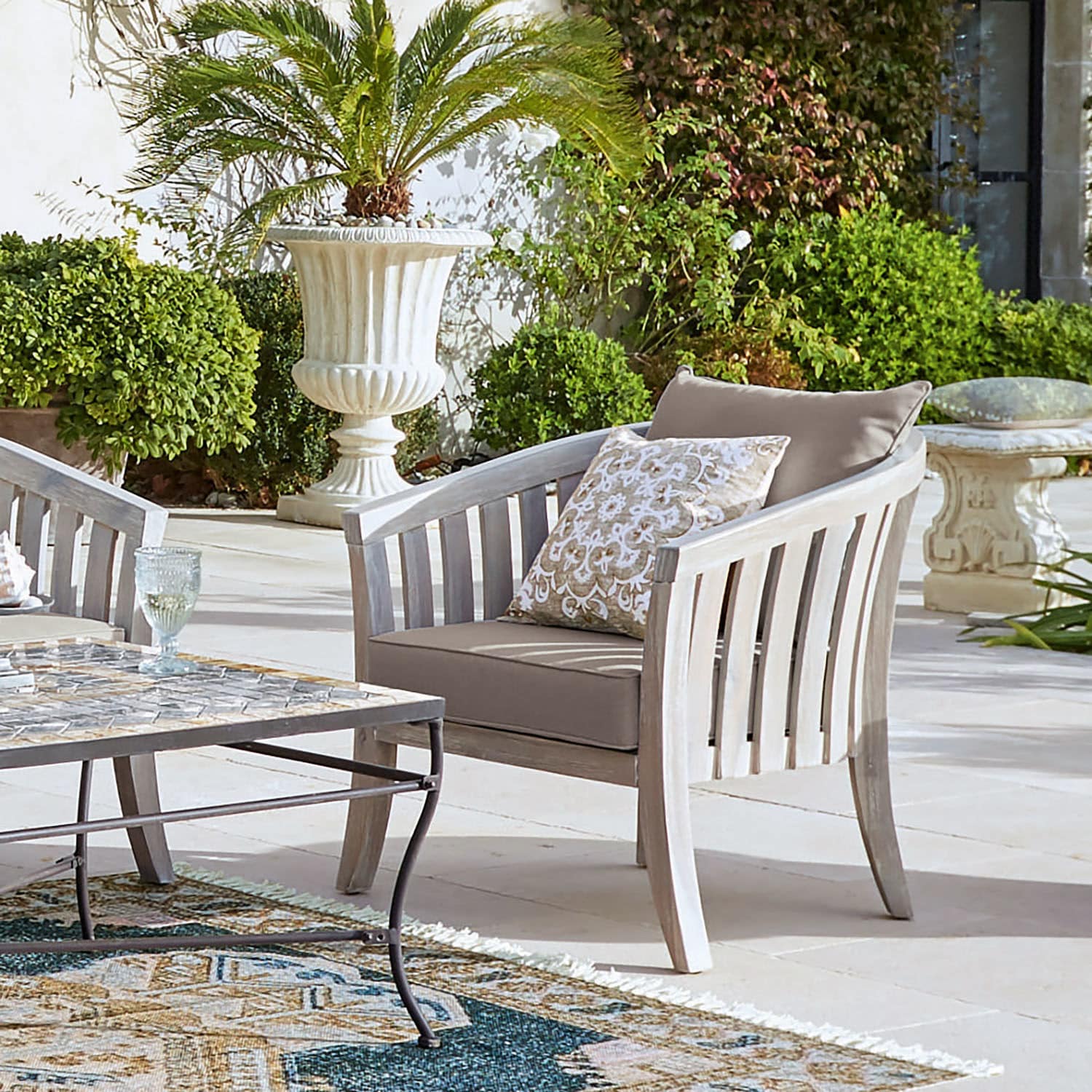 Fauteuil de jardin en bois clair avec coussins beige sur terrasse entourée de plantes vertes