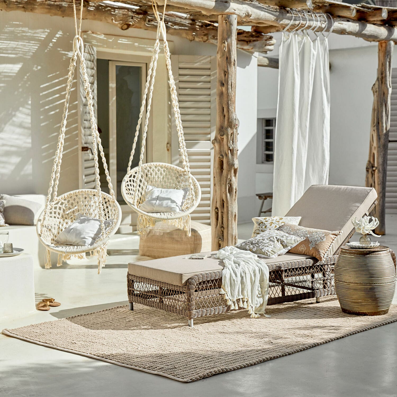 Rotan ligstoel met beige kussen en twee lichte hangstoelen van macramé buiten