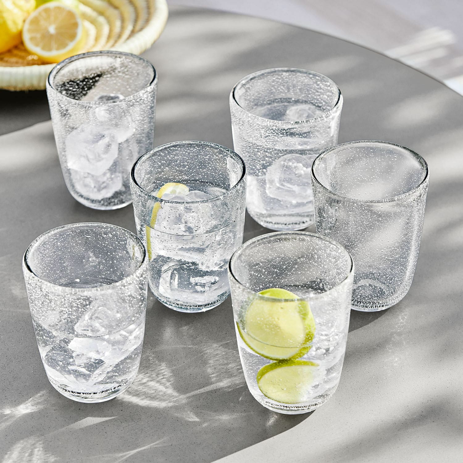 Lot de 6 verres Parilly Ensemble de six verres en verre transparent à bulles avec glaçons et tranches de citron sur table grise