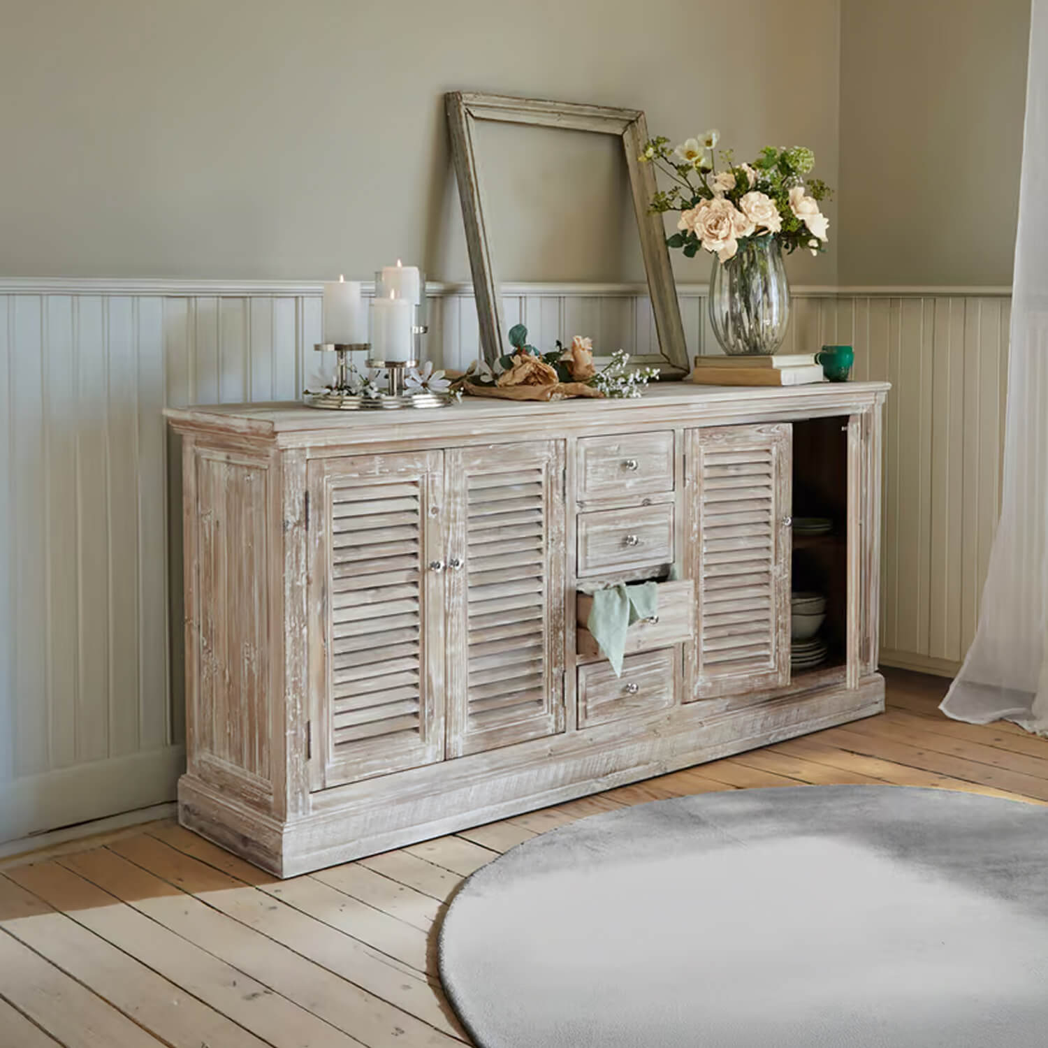Buffet rustique en bois blanc patiné avec décorations et bougies dans un salon lumineux