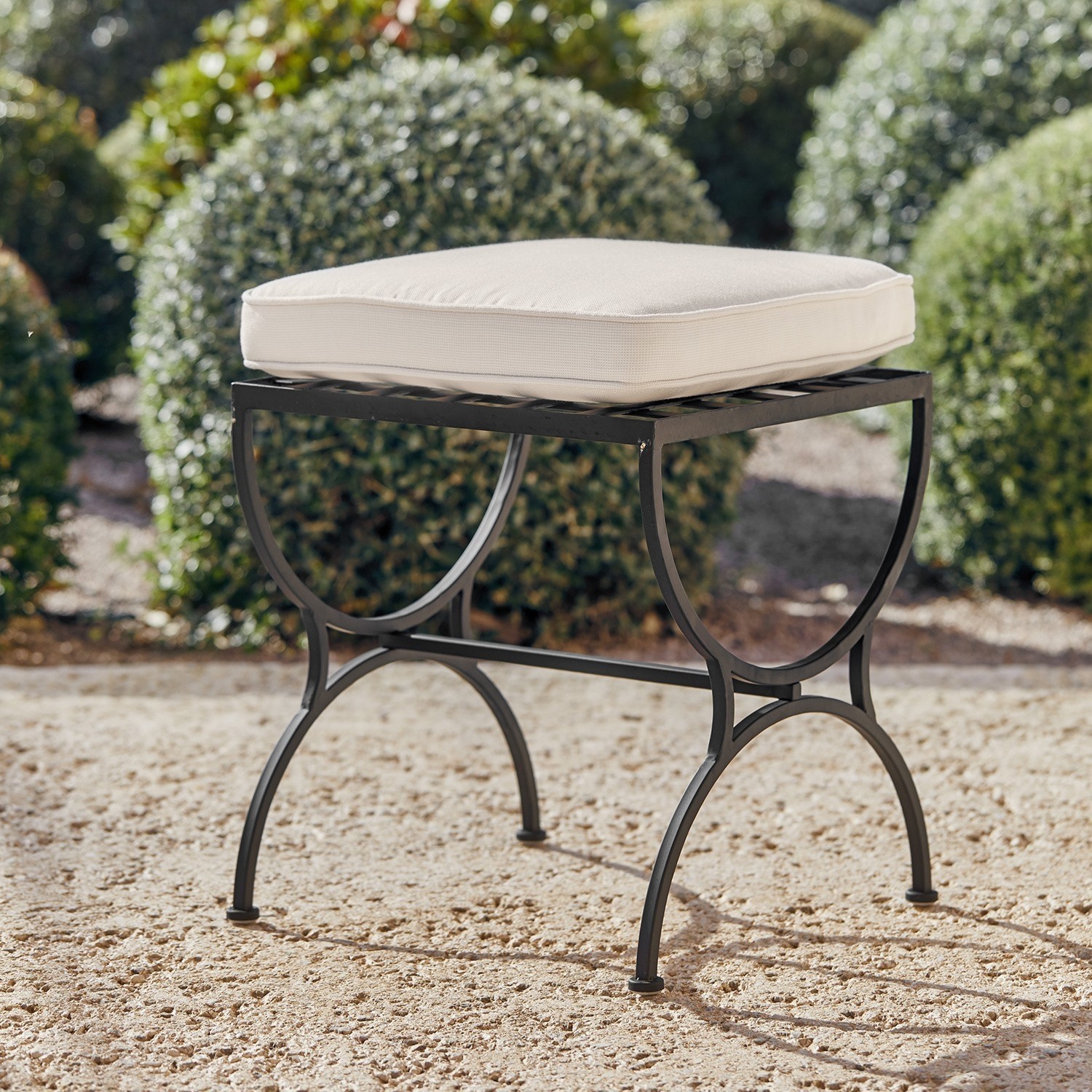 Tabouret Terell Tabouret de jardin en métal noir avec coussin crème sur sol sablonneux en extérieur
