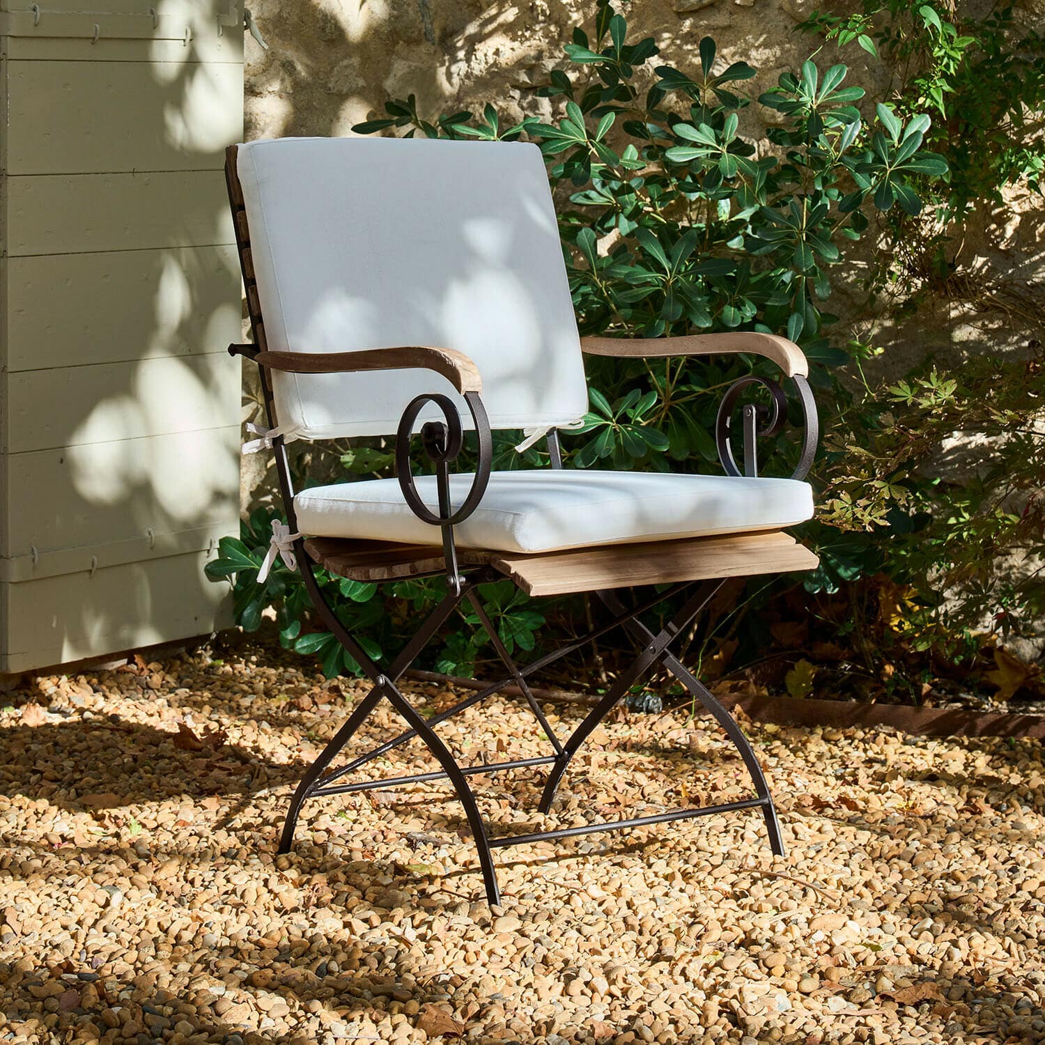 Stoel Iker Tuinstoel met metalen frame, houten armleuningen en wit kussen op grindvloer