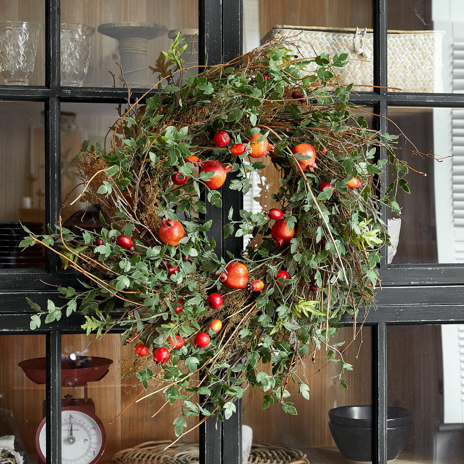 Krans Karidah Decoratieve krans van groene bladeren en rode bessen aan zwarte kastdeur, natuurlijke woondecoratie