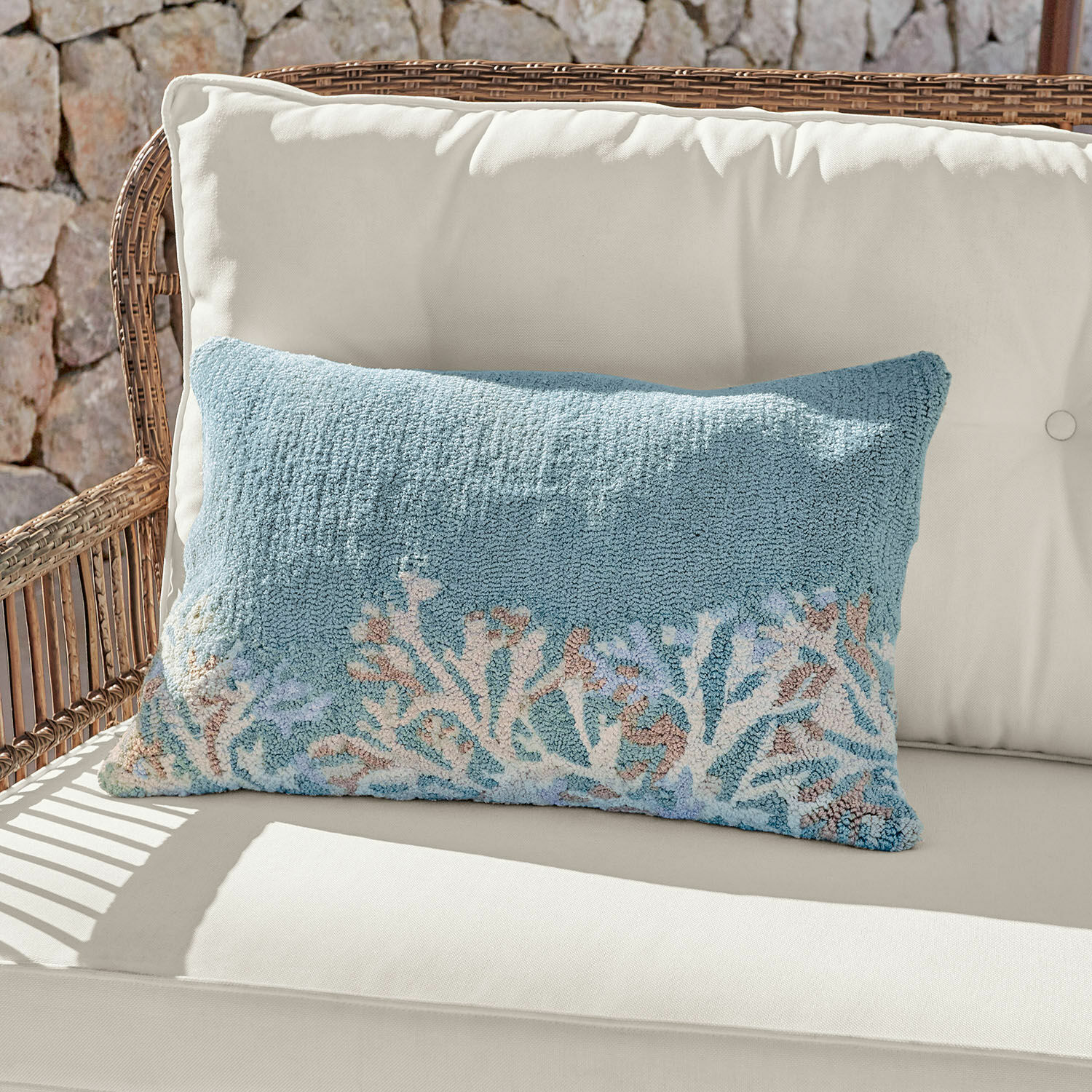 Housse de coussin d'intérieur et d'extérieur Dorlancourt Coussin décoratif bleu en tissu doux avec motif corail posé sur un canapé en rotin clair.
