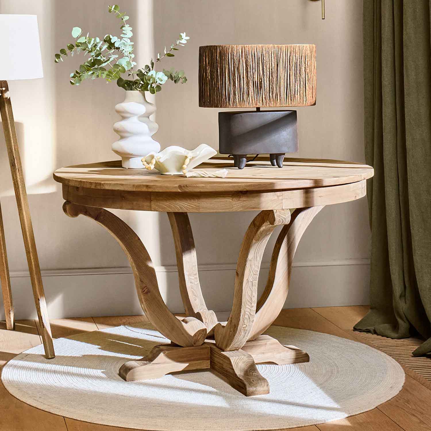 Ronde houten tafel in natuurlijke kleur met lamp en decoratieve vaas op lichte vloerkleed