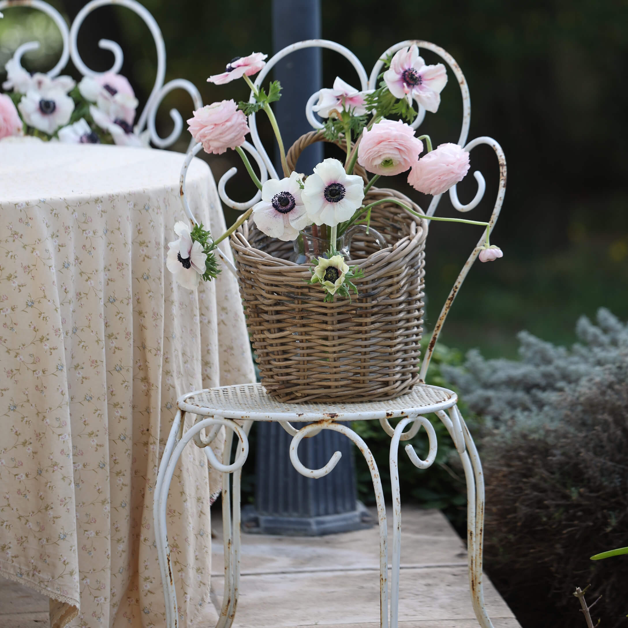 Panier en osier avec fleurs roses et blanches sur chaise en métal blanc dans un jardin