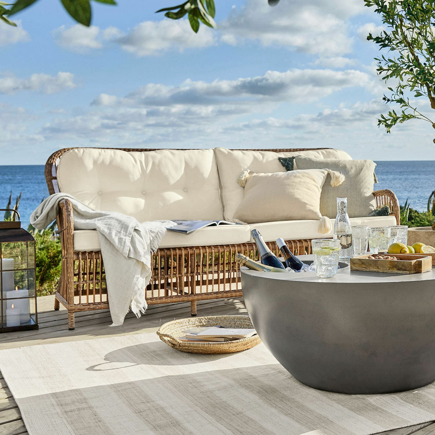 Canapé en rotin avec coussins crème sur terrasse face à la mer, mobilier d'extérieur confortable