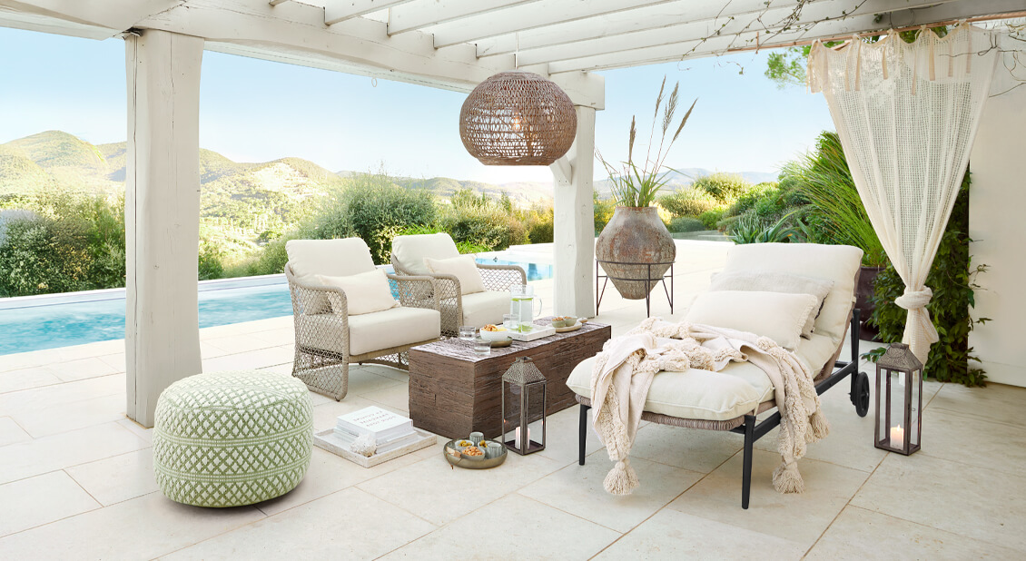Ensemble de meubles de jardin blancs avec coussins sous une pergola près de la piscine, décorations naturelles et lanternes