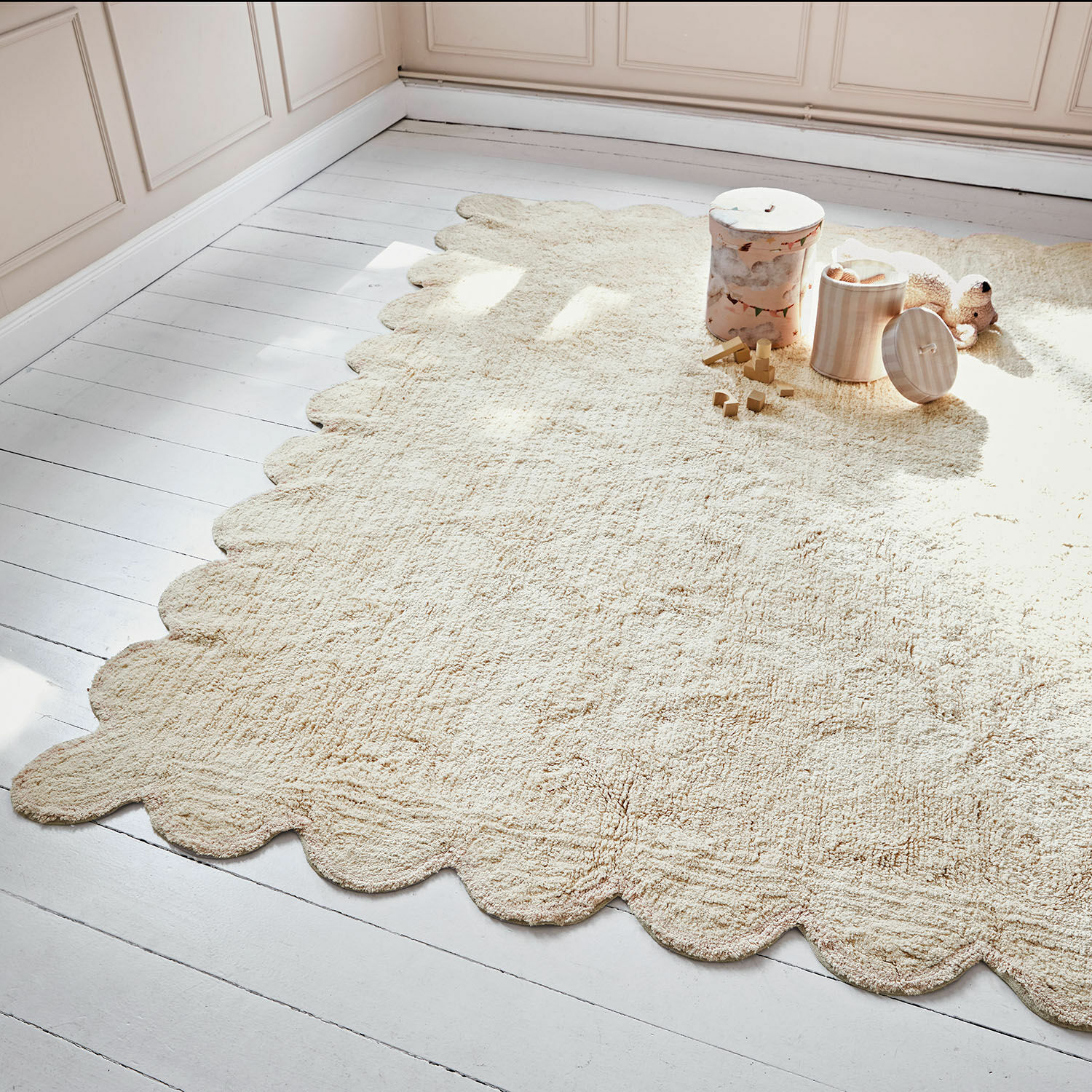 Tapis Fenvara Tapis beige en matière douce avec bord ondulé sur un sol en bois clair dans une chambre d'enfant