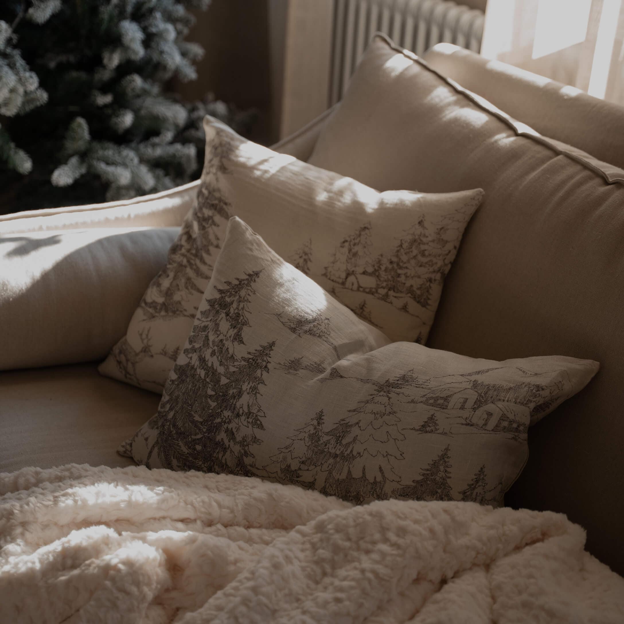 Canapé beige avec coussins imprimés forêt et couverture douce crème pour un salon chaleureux