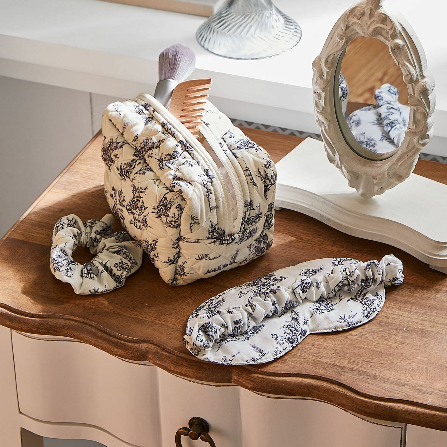 Slaapset 3-delig Felencio Beige gewatteerde make-uptas met zwart patroon, haarband en slaapmasker op houten tafel, verzorgingsaccessoires