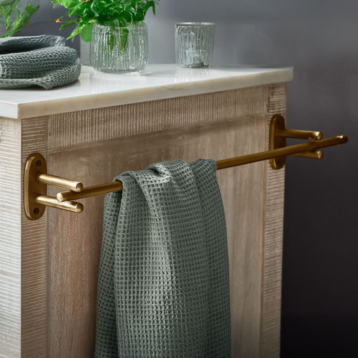 Gouden metalen handdoekhouder met groene wafelhanddoek aan houten kast met marmeren blad