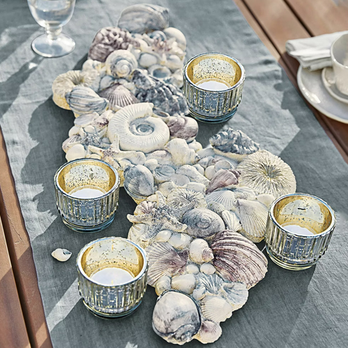 Chemin de table décoratif avec coquillages gris et quatre photophores en verre doré sur une table en bois