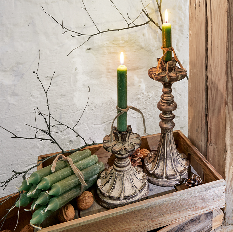 Twee decoratieve kandelaren met groene kaarsen op houten dienblad met noten en takken